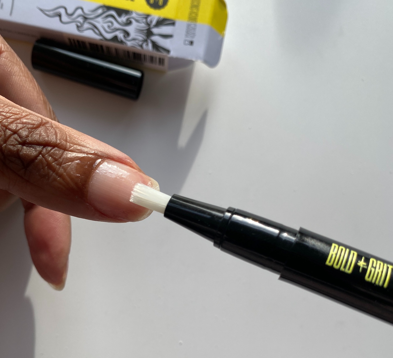 Bold&Grit nail pen being applied to brown thumb nail